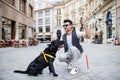 Young blind man with white cane and guide dog on pedestrain zone in city.