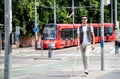 Young blind man with white cane walking across the street in city.