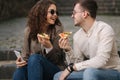 Young bloggers make selfie with slice of pizza in hands. Beautiful couple in sunglasses smile and kiss. Vegan fast food