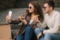 Young bloggers make selfie with slice of pizza in hands. Beautiful couple in sunglasses smile to camera phone. Vegan