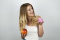 Young blond attractive woman holding juicy red apple in one hand and pink tasty cupcake in other hand isolated white Royalty Free Stock Photo