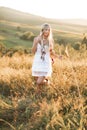 Young blond beautiful hippie girl in white dress and feather hair accessories on summer field and sunset background Royalty Free Stock Photo