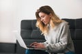 Young blond beutiful woman sits on the sofa working from home on her laptop during quarantine, cozy home atmosphere concept