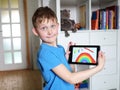 Young blond boy showing painted rainbow on tablet computer in his room. Educating and playing