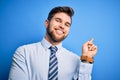 Young blond businessman with beard and blue eyes wearing elegant shirt and tie standing with a big smile on face, pointing with Royalty Free Stock Photo