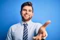 Young blond businessman with beard and blue eyes wearing elegant shirt and tie standing smiling friendly offering handshake as Royalty Free Stock Photo