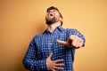 Young blond businessman with beard and blue eyes wearing shirt over yellow background laughing at you, pointing finger to the Royalty Free Stock Photo