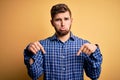 Young blond businessman with beard and blue eyes wearing shirt over yellow background Pointing down looking sad and upset, Royalty Free Stock Photo