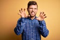 Young blond businessman with beard and blue eyes wearing shirt over yellow background smiling funny doing claw gesture as cat,