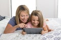 Young blond Caucasian mother lying on bed with her young sweet 7 years old daughter using internet on digital internet tablet pad Royalty Free Stock Photo