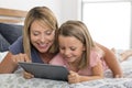 Young blond Caucasian mother lying on bed with her young sweet 7 years old daughter using internet on digital internet tablet pad Royalty Free Stock Photo