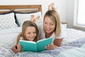 Young blond Caucasian mother lying on bed with her young sweet 7 years old daughter reading book together at home bedroom Royalty Free Stock Photo