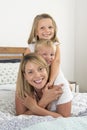 Young blond Caucasian woman lying on bed together with her little sweet 3 and 7 years old son and daughter laughing playing happy Royalty Free Stock Photo