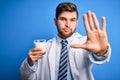 Young blond doctor man with beard and blue eyes wearing coat drinking glass of milk with open hand doing stop sign with serious