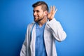 Young blond doctor man with beard and blue eyes wearing white coat and stethoscope smiling with hand over ear listening an hearing Royalty Free Stock Photo