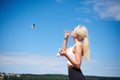 Young blond fit woman, wearing black leggings and white top,drinking water from glass bottle outside with blue sunny sky on Royalty Free Stock Photo