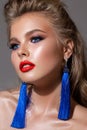 Young blond girl with bright makeup, perfect skin, volume hairdo and bright red lipstick. Blue earrings. Royalty Free Stock Photo