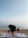 Young blond girl practice crane crow yoga asana on sea shore at sunrise