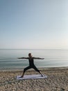 Young blond girl practice warrior yoga asana on sea shore at sunrise