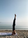 Young blond girl practice yoga headstand asana on sea shore at sunrise