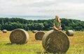 Young blond girl sitting on haystack and smiling, Hungary