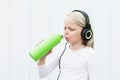 Young blond girl on white background drink fresh spring water from green reusable bottle.