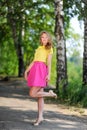 Young blond girl in yellow blouse with bright pink skirt posing in summer park