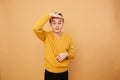 Young blond guy dressed in yellow sweater keeps his fingers above his eyebrows on the beige background in the studio Royalty Free Stock Photo