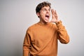 Young blond handsome man with curly hair wearing casual sweater over white background shouting and screaming loud to side with Royalty Free Stock Photo