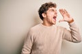 Young blond handsome man with curly hair wearing casual sweater over white background shouting and screaming loud to side with Royalty Free Stock Photo