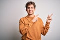 Young blond handsome man with curly hair wearing casual sweater over white background smiling and looking at the camera pointing Royalty Free Stock Photo