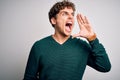 Young blond handsome man with curly hair wearing green sweater over white background shouting and screaming loud to side with hand Royalty Free Stock Photo