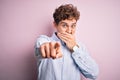 Young blond handsome man with curly hair wearing striped shirt over white background laughing at you, pointing finger to the Royalty Free Stock Photo