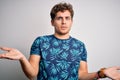 Young blond handsome man on vacation with curly hair wearing casual summer t-shirt clueless and confused with open arms, no idea Royalty Free Stock Photo