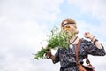 Young blond hippie woman, wearing grey boho style dress and yellow sunglasses, standing on green field, holding camomile bouquet, Royalty Free Stock Photo