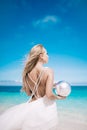 Young blond long hair bride wear a white open back wedding dress and stand on the white sand beach with a pearl. Looking to the se Royalty Free Stock Photo