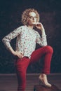 A young blond man androgyn in the image of an attractive woman dressed in a floral shirt, posing sitting on a chair, one hand Royalty Free Stock Photo