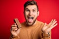 Young blond man with beard and blue eyes eating healthy chocolate protein bar very happy and excited, winner expression Royalty Free Stock Photo