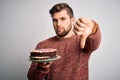 Young blond man with beard and blue eyes holding birthday cake over white background with angry face, negative sign showing Royalty Free Stock Photo