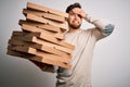 Young blond man with beard and blue eyes holding cardboards of pizza over white background stressed with hand on head, shocked