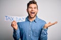 Young blond man with beard and blue eyes holding paper with tax day message very happy and excited, winner expression celebrating Royalty Free Stock Photo