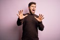 Young blond man with beard and blue eyes wearing casual sweater over pink background afraid and terrified with fear expression Royalty Free Stock Photo