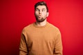 Young blond man with beard and blue eyes wearing casual sweater over red background making fish face with lips, crazy and comical Royalty Free Stock Photo