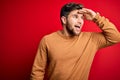 Young blond man with beard and blue eyes wearing casual sweater over red background very happy and smiling looking far away with Royalty Free Stock Photo