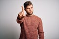 Young blond man with beard and blue eyes wearing casual sweater over white background Pointing with finger up and angry Royalty Free Stock Photo