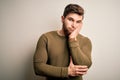 Young blond man with beard and blue eyes wearing green sweater over white background thinking looking tired and bored with Royalty Free Stock Photo