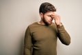Young blond man with beard and blue eyes wearing green sweater over white background tired rubbing nose and eyes feeling fatigue Royalty Free Stock Photo