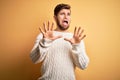 Young blond man with beard and blue eyes wearing white sweater over yellow background afraid and terrified with fear expression Royalty Free Stock Photo