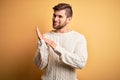 Young blond man with beard and blue eyes wearing white sweater over yellow background clapping and applauding happy and joyful, Royalty Free Stock Photo