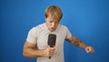 A young blond man with a beard singing into a hairbrush on a blue background Royalty Free Stock Photo